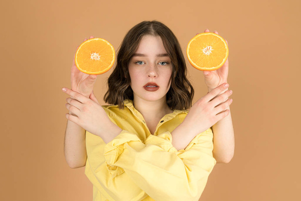 Beauty portrait of attractive young girl with healthy skin and red lips, female looking at the camera and holds strangers hands with sliced orange - Foto, afbeelding