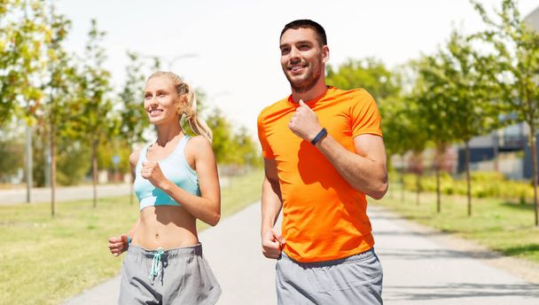 ευτυχισμένο ζευγάρι με fitness trackers που τρέχουν σε εξωτερικούς χώρους - Φωτογραφία, εικόνα