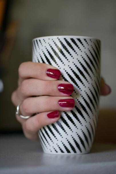 Mano femenina con uñas rojas sosteniendo taza de té grande
 - Foto, imagen