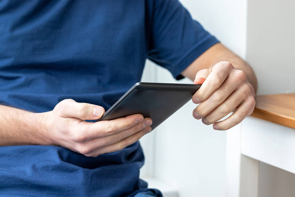Libro electrónico gris e-reader en manos masculinas. Un hombre con una camiseta azul con una tableta. Enfoque selectivo
 - Foto, imagen