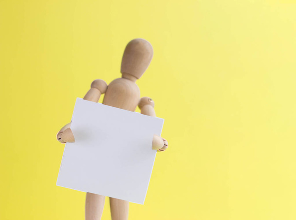 Wooden mannequin holds in hand a blank bulletin board. wooden dummy presents your business. copy space for text or advertising - Foto, Imagem