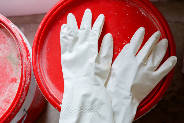 Kullanılmış beyaz lateks eldivenler bir boya kovasının kırmızı kapağında yatıyor. - Fotoğraf, Görsel
