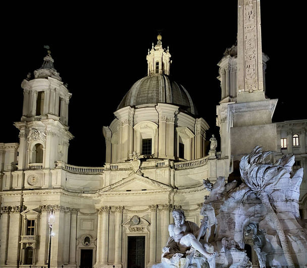 Nachtaufnahme der beleuchteten Fassade der Barockkirche Sant 'Agnese in Agone mit dem Brunnen der vier Flüsse auf der Piazza Navona in Rom - Foto, Bild