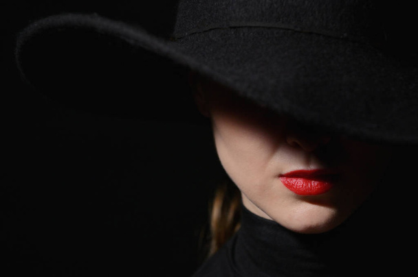 Nainen, jolla on punaiset huulet mustassa hatussa mustalla taustalla
 - Valokuva, kuva