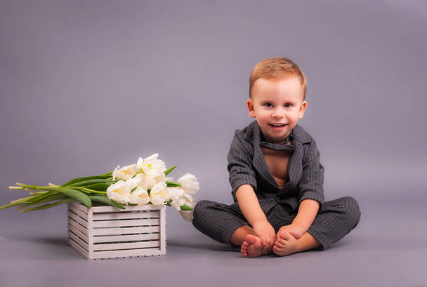A little gentleman with a bouquet of tulips in the Studio on a gray background in honor of the women's holiday on March 8 and a greeting card in the form of all mothers, grandmothers, girls, girls - Фото, зображення