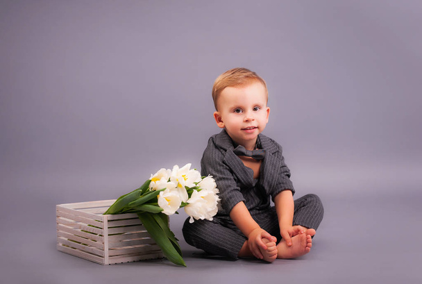 A little gentleman with a bouquet of tulips in the Studio on a gray background in honor of the women's holiday on March 8 and a greeting card in the form of all mothers, grandmothers, girls, girls - Photo, Image