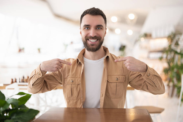Young handsome bearded man pointing at himself with both fingers while sitting in the cafe , body language concept. - Foto, Imagen