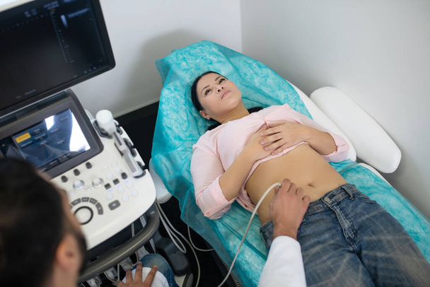 Asian woman laying on the couch having ultrasonic investigation of abdomen - Fotografie, Obrázek