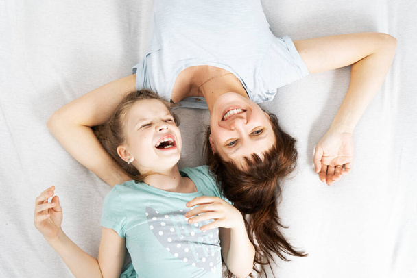 Семейное время: мама и дочь лежат на кровати обнимаясь и весело смеясь. - Фото, изображение