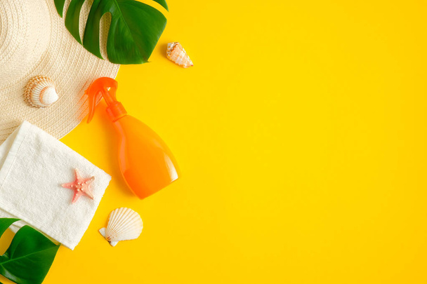Sunscreen spray bottle on yellow background with beach hat and tropical leaves. Top view with copy space. Sun protection cosmetic products, summer skin care concept - Φωτογραφία, εικόνα