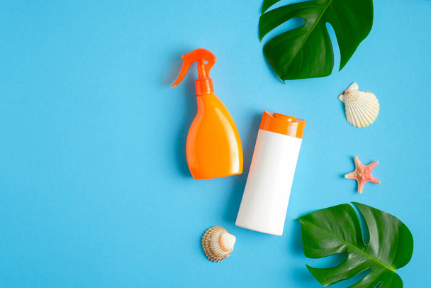 Sunscreen lotion bottle and sunblock spray package on blue background with tropical leaves and seashells. Top view with copy space. Sun protection cosmetic products, summer skin care concept - Photo, image