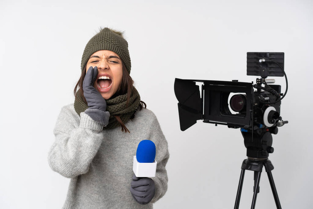 Δημοσιογράφος γυναίκα κρατώντας ένα μικρόφωνο και αναφέροντας ειδήσεις πάνω από απομονωμένο λευκό φόντο φωνάζοντας και ανακοινώνοντας κάτι - Φωτογραφία, εικόνα