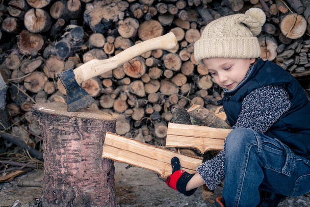 One little boy chopping firewood in the front yard at the day time. Kid having fun outdoors. Concept happy lifestyle. - Фото, изображение
