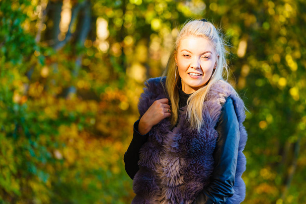 Woman wearing fashionable outfit artificial fur coat walking in autumnal park. - Фото, зображення