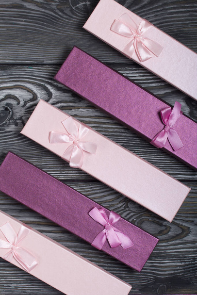 Cardboard boxes with gifts. Pink and lilac, decorated with ribbon bows. Lying on the background of brushed pine boards. - Foto, imagen