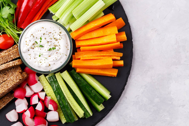 Zdravá zeleninová svačinka s jogurtovou omáčkou na břidlicové desce, horní pohled zblízka, kopírovací prostor - Fotografie, Obrázek