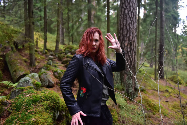 red-haired woman in a black leather jacket in the forest - Foto, imagen