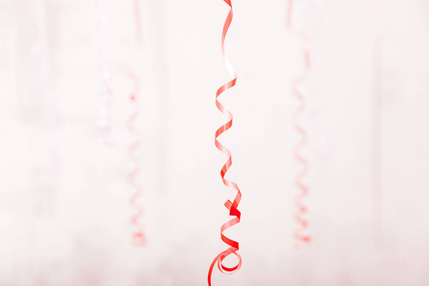 copy space with red curly ribbon serpentine hanging in a room among other pink curly defocused ribbons on fair pink background - Valokuva, kuva