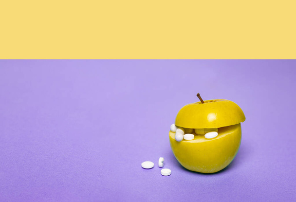 Medicine concept with fresh apple and tablets in its cut. Genetically modified fruit on purple and yellow background. Copy space, place for text, horizontal. - Fotó, kép