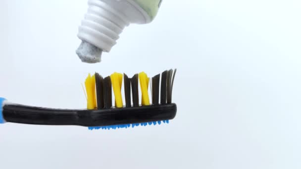 A pasta de dentes azul com manchas de carbono é suavemente espremida para fora do tubo em uma escova azul escura. Macro vídeo de cerdas e textura pasta de dentes. Conceito de Cuidado Oral
. - Filmagem, Vídeo
