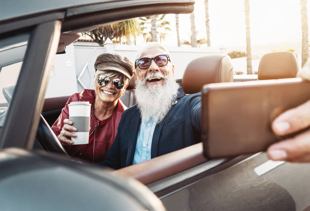Szczęśliwa para seniorów biorąc selfie na nowy nowoczesny samochód kabrioletowy - Dojrzałe osoby bawiące się razem co zdjęcia siebie podczas podróży samochodem wakacje - Starszego stylu życia i transportu koncepcja - Zdjęcie, obraz
