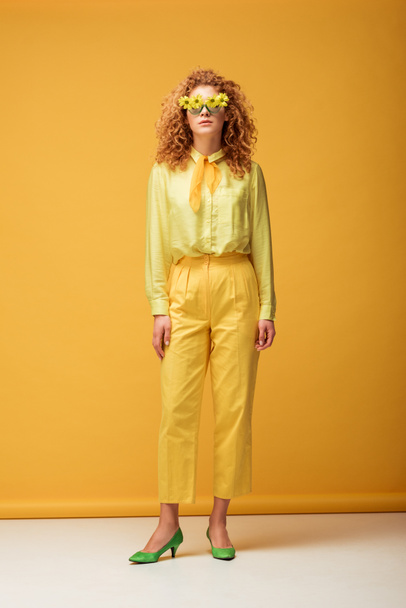 curly redhead woman in sunglasses with flowers posing on yellow  - Foto, Bild