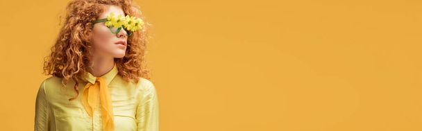 panoramic shot of stylish redhead woman in sunglasses with flowers isolated on yellow  - Fotó, kép
