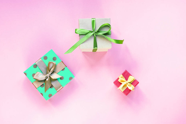 Drei Geschenke in Schachteln mit Schleifenknoten auf rosa Hintergrund. Frühjahrsferien, Geburtstagskonzept. Draufsicht, flache Lage. - Foto, Bild