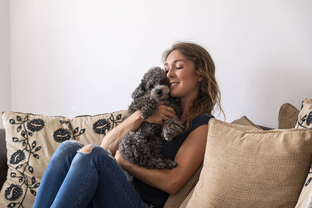 молодая женщина, сидящая на диване, обнимаясь щенок какапу
 - Фото, изображение