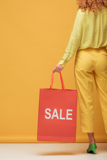 back view of stylish redhead woman holding shopping bag with sale lettering on yellow  - Foto, imagen