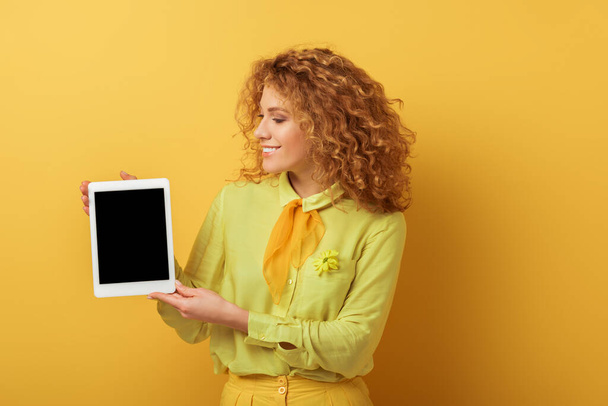 allegra rossa donna in possesso di tablet digitale con schermo bianco isolato su giallo
  - Foto, immagini