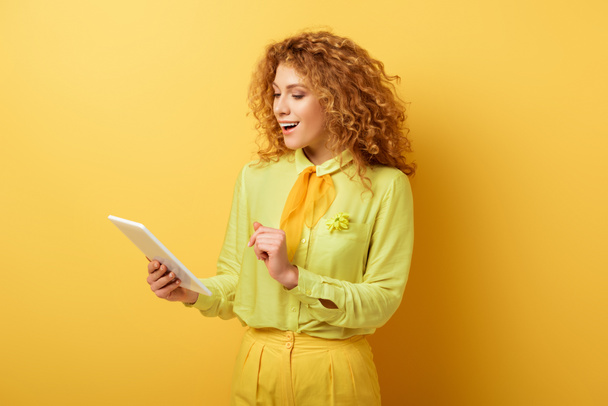 happy redhead girl looking at digital tablet on yellow  - Foto, imagen