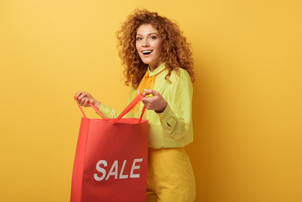 heureuse rousse femme tenant sac à provisions avec vente lettrage sur jaune
  - Photo, image