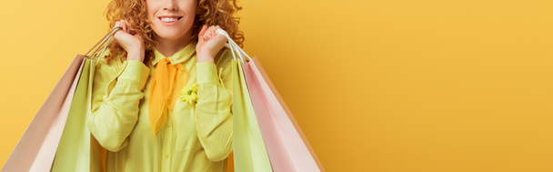 panoramic shot of happy redhead woman holding shopping bags on yellow  - Photo, Image