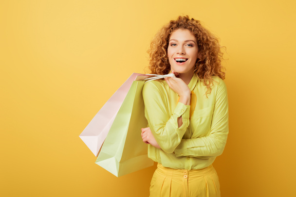 mujer pensativa y rizada sosteniendo bolsas de compras en amarillo
  - Foto, imagen