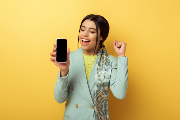 felice ragazza afro-americana che tiene smartphone con schermo bianco e celebra sul giallo
  - Foto, immagini