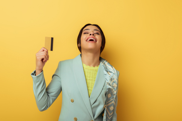 happy african american girl laughing and holding credit card on yellow  - Φωτογραφία, εικόνα