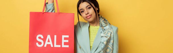 panoramic shot of attractive african american girl holding shopping bag with sale lettering on yellow  - Fotografie, Obrázek