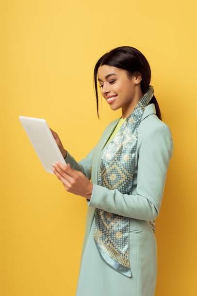 gelukkig Afrikaans amerikaanse vrouw met behulp van digitale tablet geïsoleerd op geel  - Foto, afbeelding