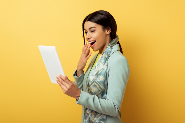 mulher americana africana feliz cobrindo a boca e olhando para tablet digital em amarelo
  - Foto, Imagem
