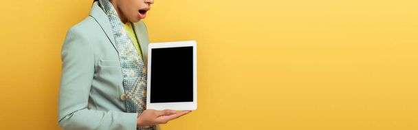tiro panorâmico de mulher afro-americana chocada segurando tablet digital com tela em branco isolado no amarelo
  - Foto, Imagem
