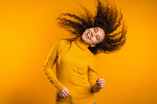Mixed race woman portrait with big afro curly hair on yellow background dancing and with hairstyle flying in air - Photo, image