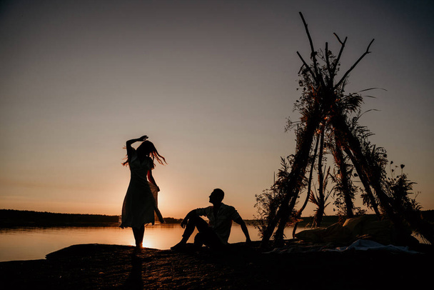 Una pareja joven se está abrazando en el agua en Sunset. Dos siluetas contra el sol. Historia de amor romántica. Wigwam en la piedra
. - Foto, imagen