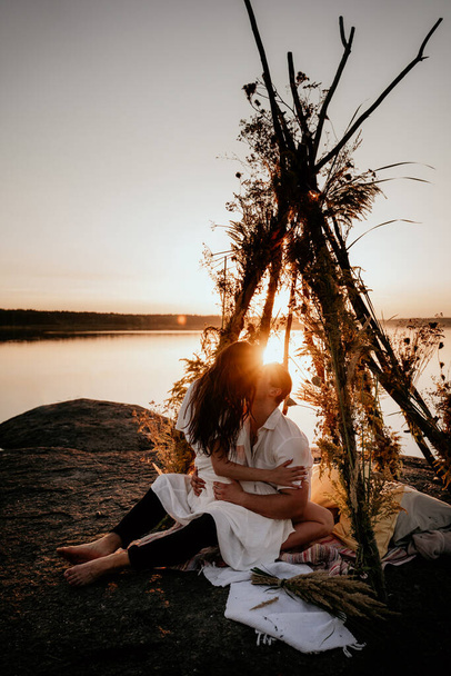 Young couple is embracing and kissing in wigwam on the coast. Romantic love story. Idea for photosession. - Photo, image