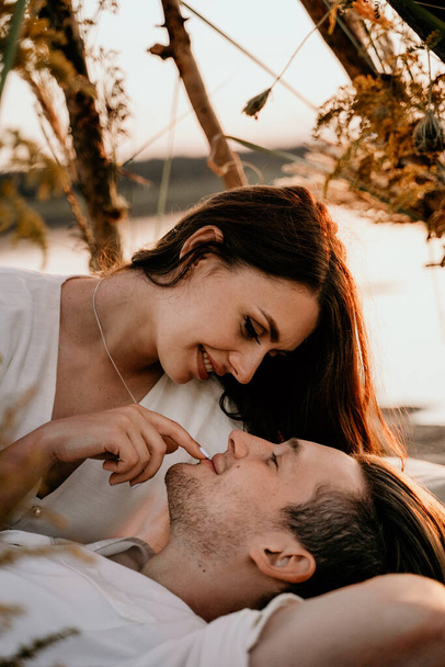 Νεαρό ζευγάρι αγκαλιάζεται και φιλιέται στην ακτή Σάνσετ. Ρομαντική ιστορία αγάπης. Μελαχρινή με ελαφρύ φόρεμα.. - Φωτογραφία, εικόνα