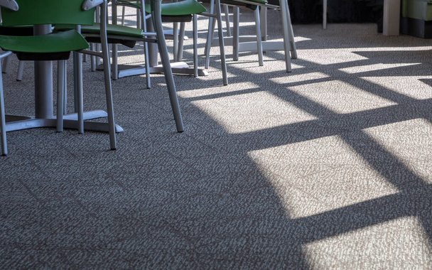 Sonnenstrahl aus einem Fenster in einem luftigen Café schafft ein Muster auf diesem grauen Teppichboden - Foto, Bild