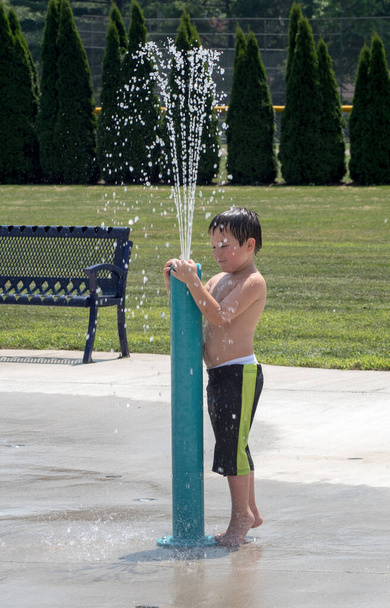 Young boy in bathing shorts cools off in an urban splash pad fountain for kids - Photo, Image