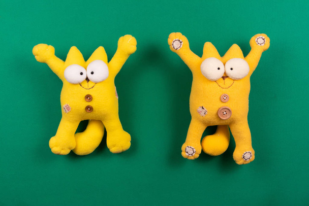 Két vicces barátságos mosolygós sárga macskák nyitott mancsok ellen zöld háttér, designer puha játékok - Fotó, kép