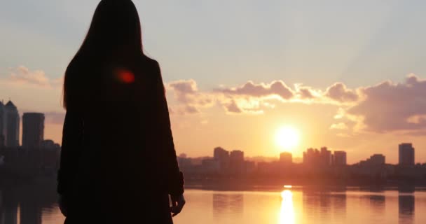 Silueta de mujer con las manos levantadas mirando el amanecer del paisaje urbano
 - Imágenes, Vídeo