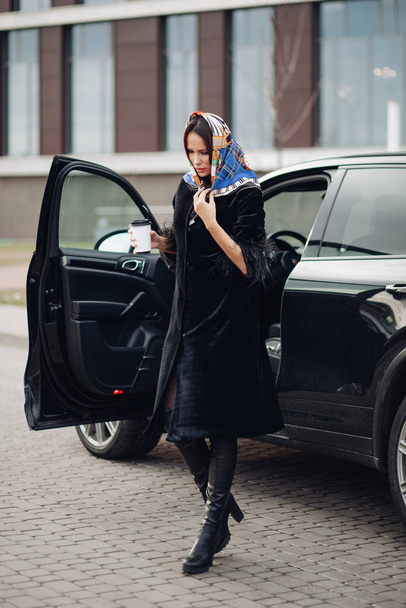 Κομψό πλούσια γυναίκα με φλιτζάνι καφέ δίπλα στο αυτοκίνητό της. - Φωτογραφία, εικόνα